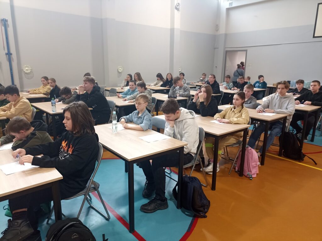 Uczniowie piszący test na sali gimnastycznej podczas eliminacji gminnych XLVII Ogólnopolskiego Turnieju Wiedzy Pożarniczej "Młodzież zapobiega pożarom"