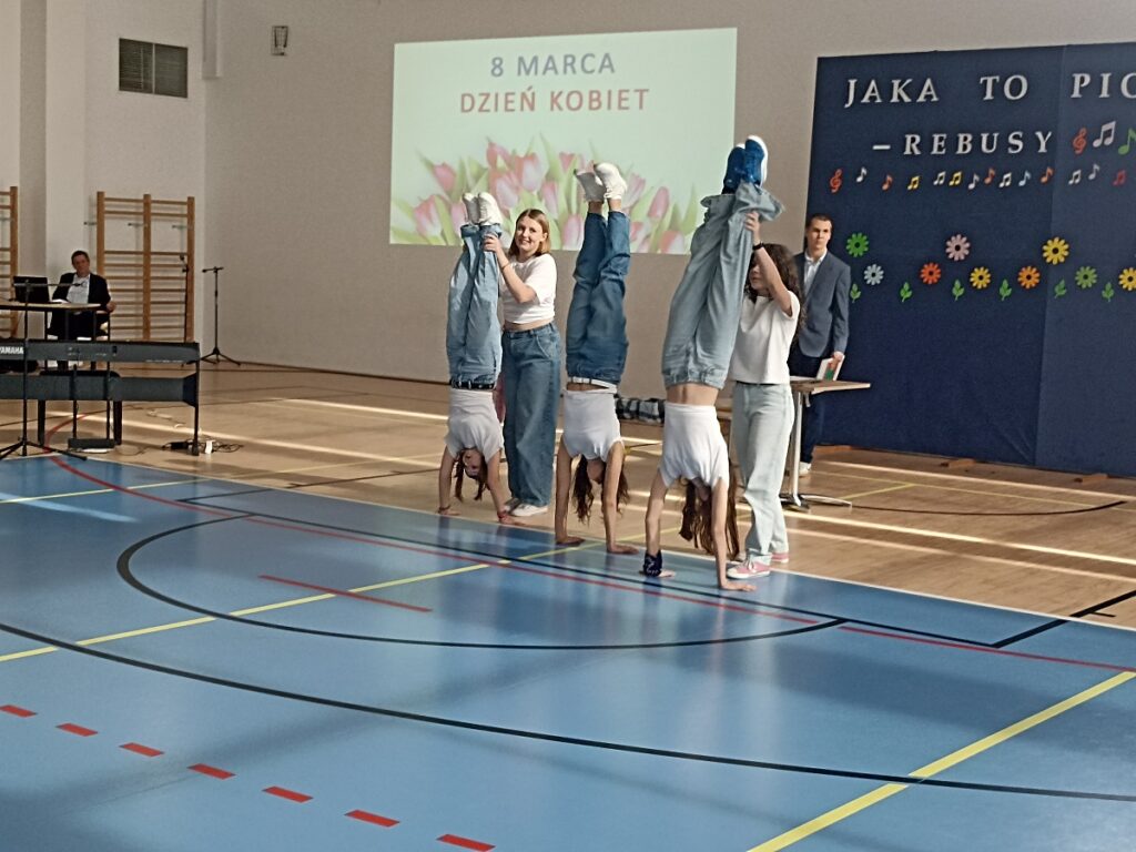 Pięć dziewcząt, które tańczą w rytm piosenki podczas akademii z okazji Dnia Kobiet w PSP nr 3 z O. I. w Kozienicach. Trzy uczennice stoją na rękach, pozostałe dwie je asekurują