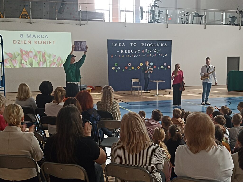 Występujący uczniowie na akademii z okazji Dnia Kobiet w PSP nr 3 z O. I. w Kozienicach. Na pierwszym planie tyłem kadra pedagogiczna i uczniowie szkoły