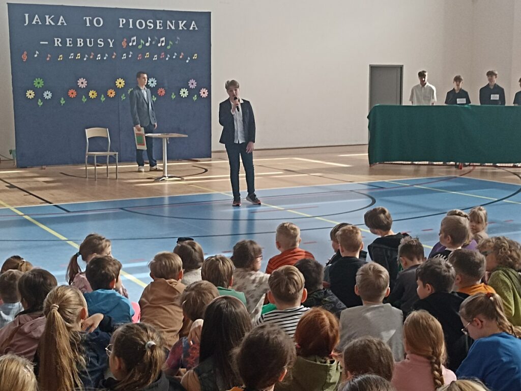 Występujący uczeń na akademii z okazji Dnia Kobiet w PSP nr 3 z O. I. w Kozienicach. W tle inni uczniowie.