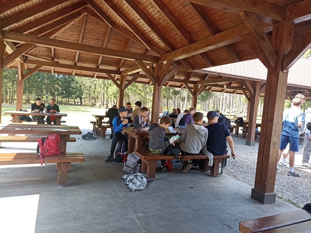 Grupa siedzących uczniów z PSP 3 Kozienice podczas rajdu pieszego do "Królewskich Źródeł"